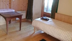 Una habitació de fusta amb un llit, una taula i una finestra amb cortines.