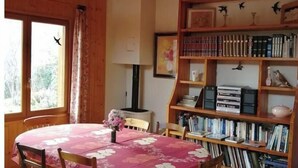 Una habitació acollidora amb una taula de fusta i cadires, una estanteria plena de llibres i una finestra amb cortines.
