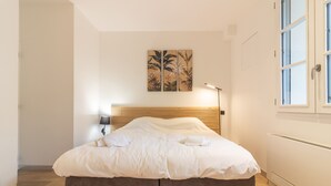 Ein ordentlich bezogenes Bett mit einem Holz-Kopfteil, einer Wandlampe und einem Kunstwerk im tropischen Stil darüber.