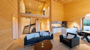 A spacious wooden interior with a central living area featuring a sofa, a coffee table, and a staircase leading to an upper level. - 50 - Gallery Chalet "Josephine" (Daun)