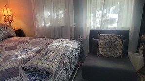 A bedroom with a bed, a chair, a lamp, and a window with sheer curtains. - Urban Farm House +Hot Tub+Pool (Long Beach)