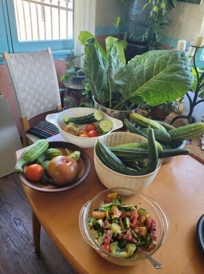 A table with various vegetables, a bowl of salad, and a chair with a woven seat.
