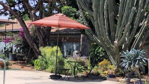 A pool area with a tiled edge, a red umbrella, and various plants including cacti. - Urban Farm House +Hot Tub+Pool (Long Beach)