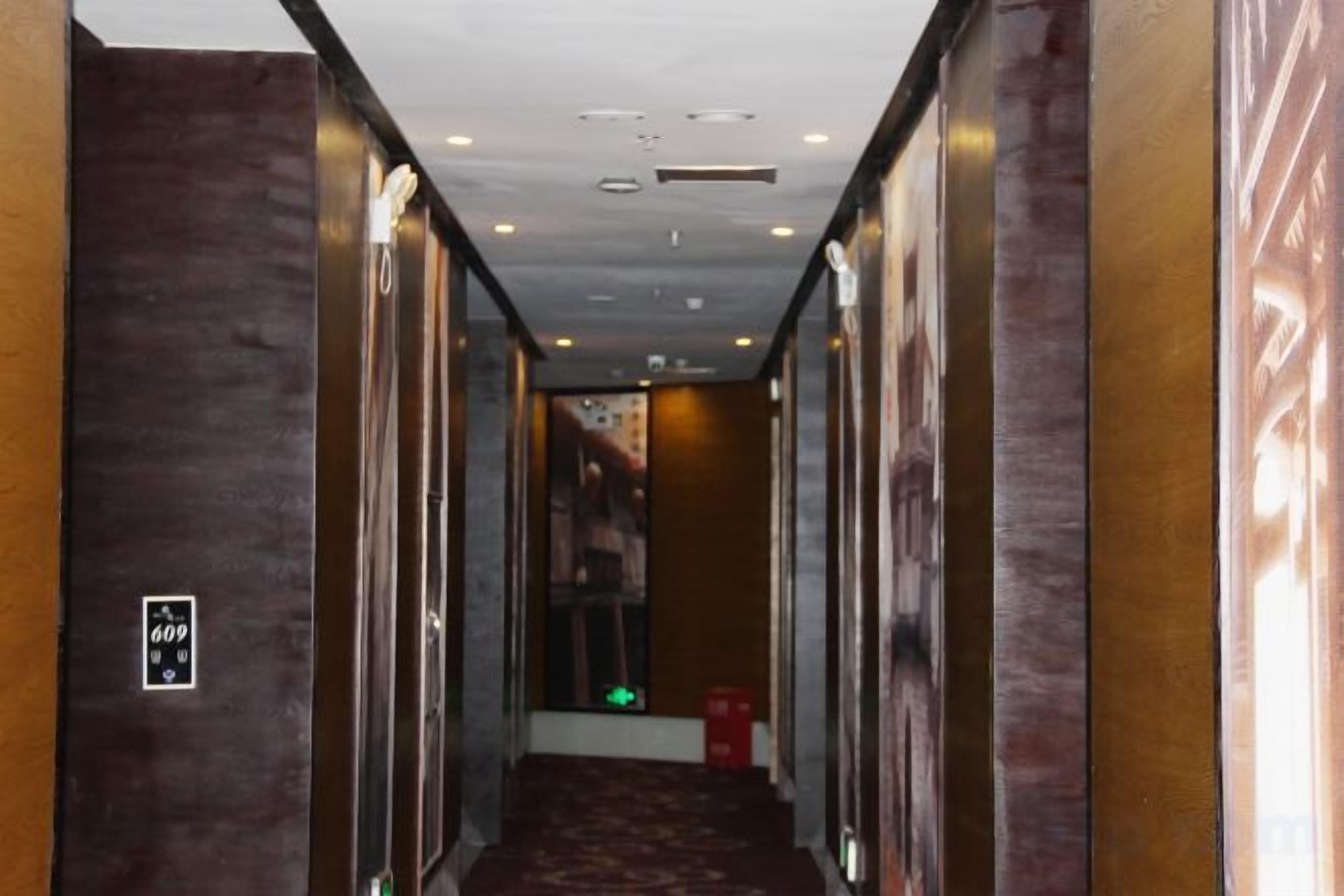 A hallway with a carpeted floor, a wall-mounted elevator button, and a trash bin.