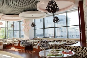 A modern interior with round tables and benches, large windows, and decorative ceiling lights.
