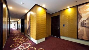 A hotel corridor with a red carpet, walls with a textured pattern, and a door with a sign.