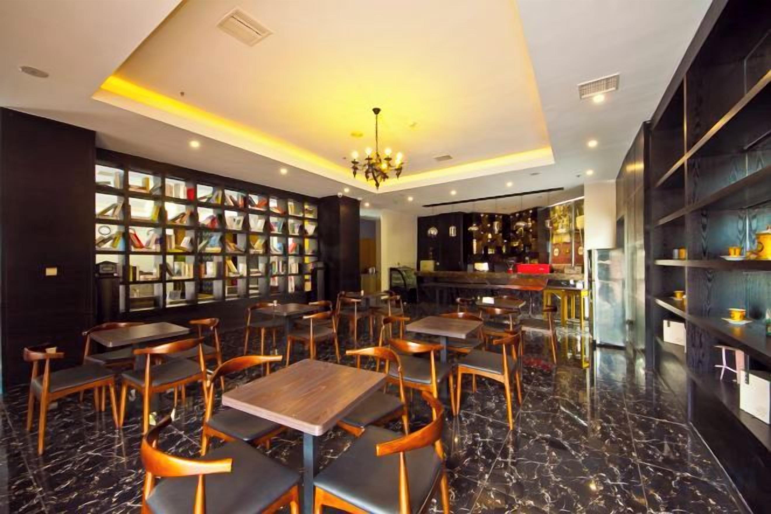 A restaurant with marble flooring, wooden tables and chairs, a chandelier, and a bookshelf filled with books.