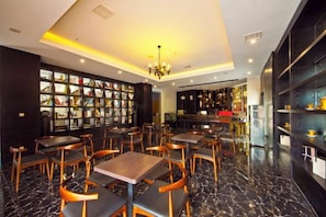 A restaurant with marble flooring, wooden tables and chairs, a chandelier, and a bookshelf filled with books.