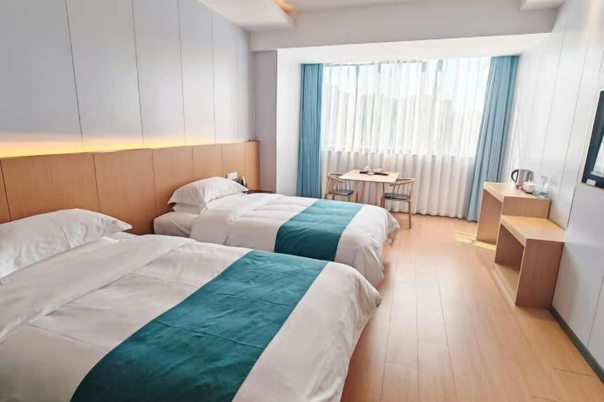 Hotellihuone, jossa on kaksi sänkyä, pieni pöytä, tuoleja, työpöytä ja ikkuna, jossa on verhot.