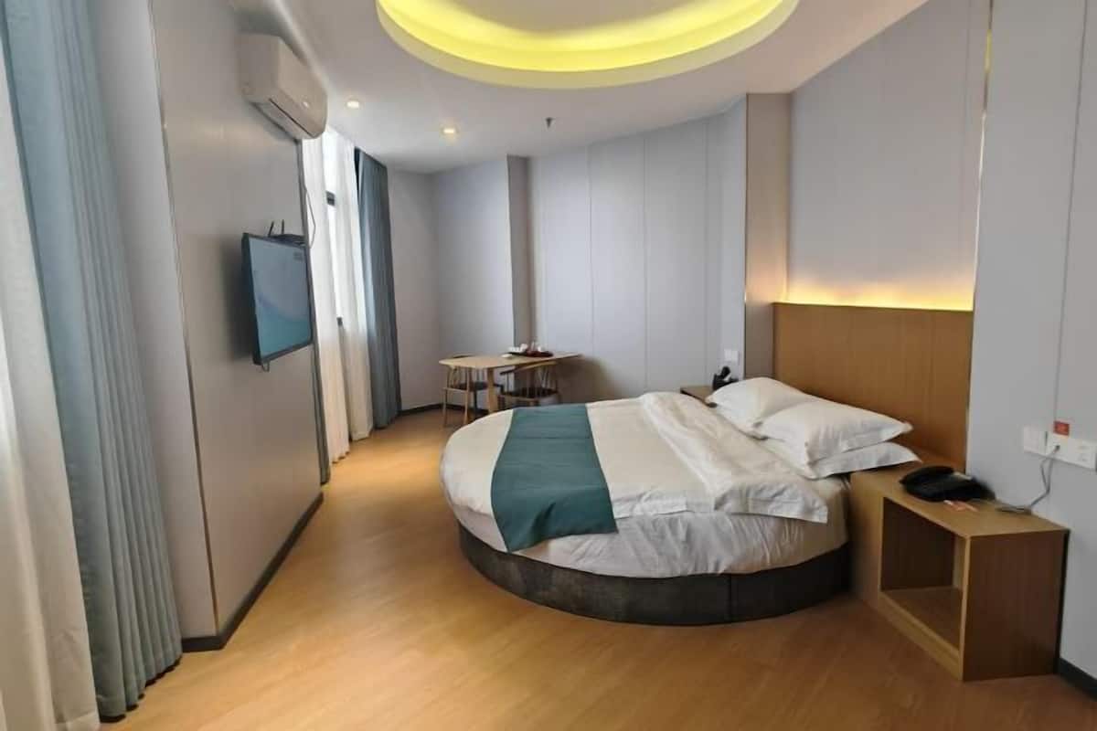 Moderni hotellihuone, jossa on kaareva sänky, pieni työpöytä, televisio ja kattovalaisin.