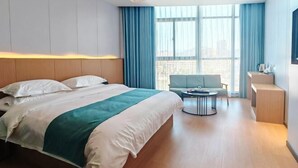 A modern hotel room with a large bed, a seating area with a table, and a view of the city through large windows.