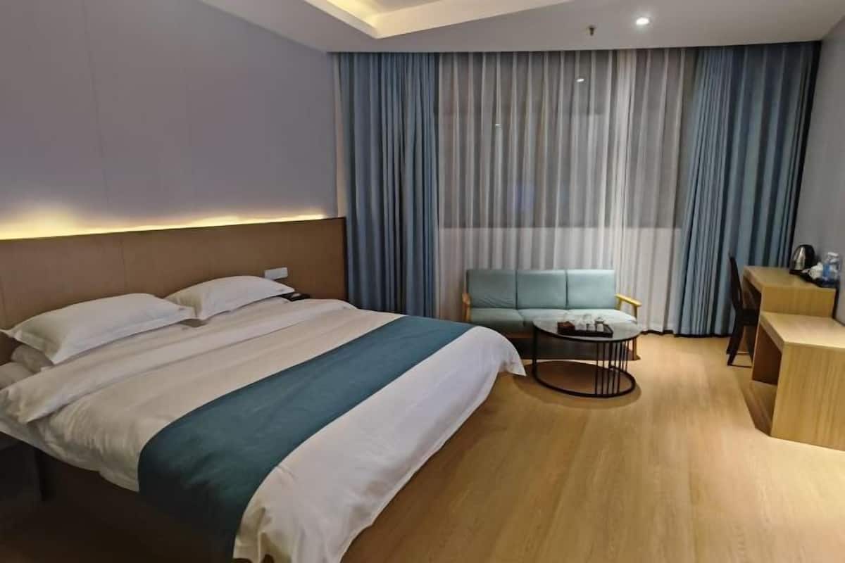 Hotellihuone, jossa on sänky, oleskelualue, jossa on tuoli ja pieni pöytä, sekä työpöytä tuolilla.