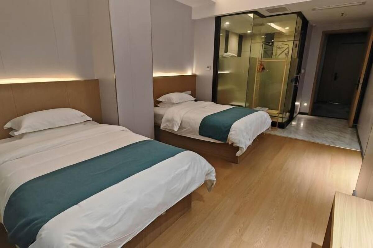 Hotellihuone, jossa on kaksi sänkyä, lasinen suihkuseinä ja puulattia.