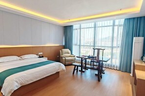 A hotel room with a large bed, a desk, a chair, and a view of the city through large windows. - Yanlin Culture Hotel (Shaowu)