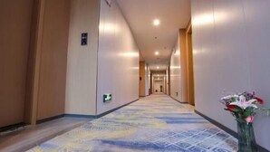 A hotel hallway with a patterned carpet, wooden walls, and a vase of flowers.