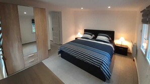 Une chambre à coucher comprenant un lit, des tables de chevet, une armoire et un miroir.