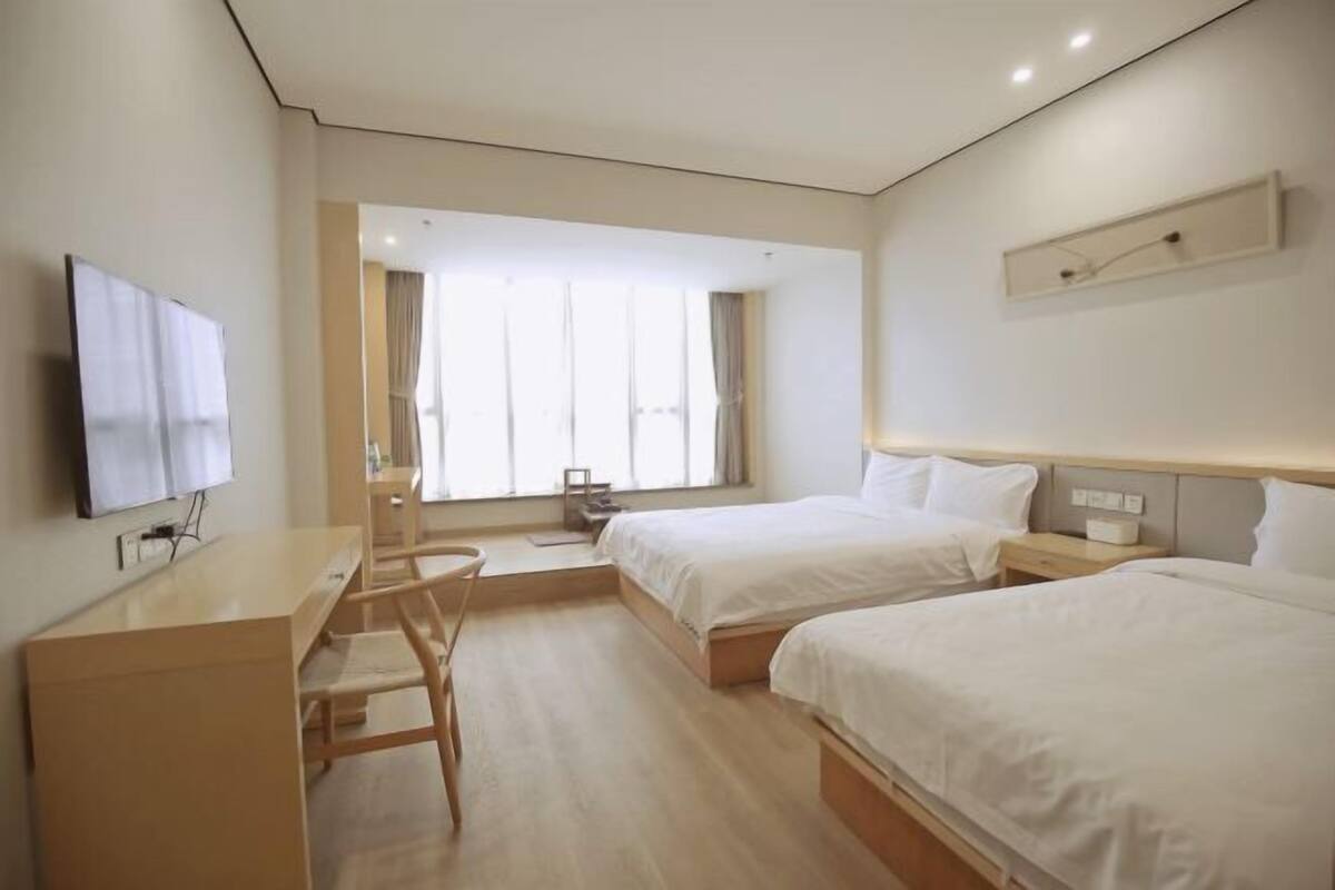 Habitación de hotel con dos camas, un escritorio, una silla y un televisor.