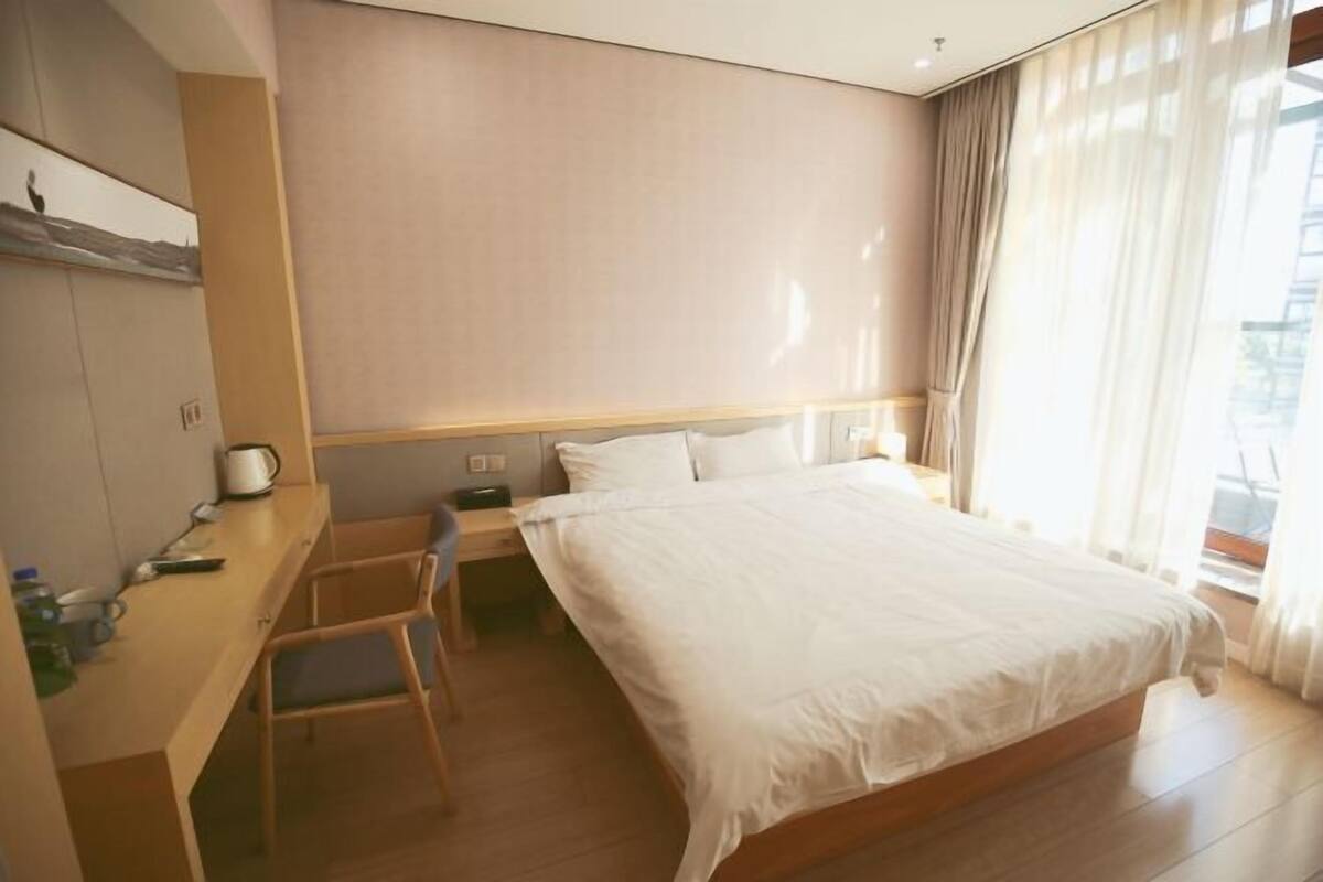 Una habitación de hotel con cama, escritorio, silla, mesita de noche y ventana con cortinas.