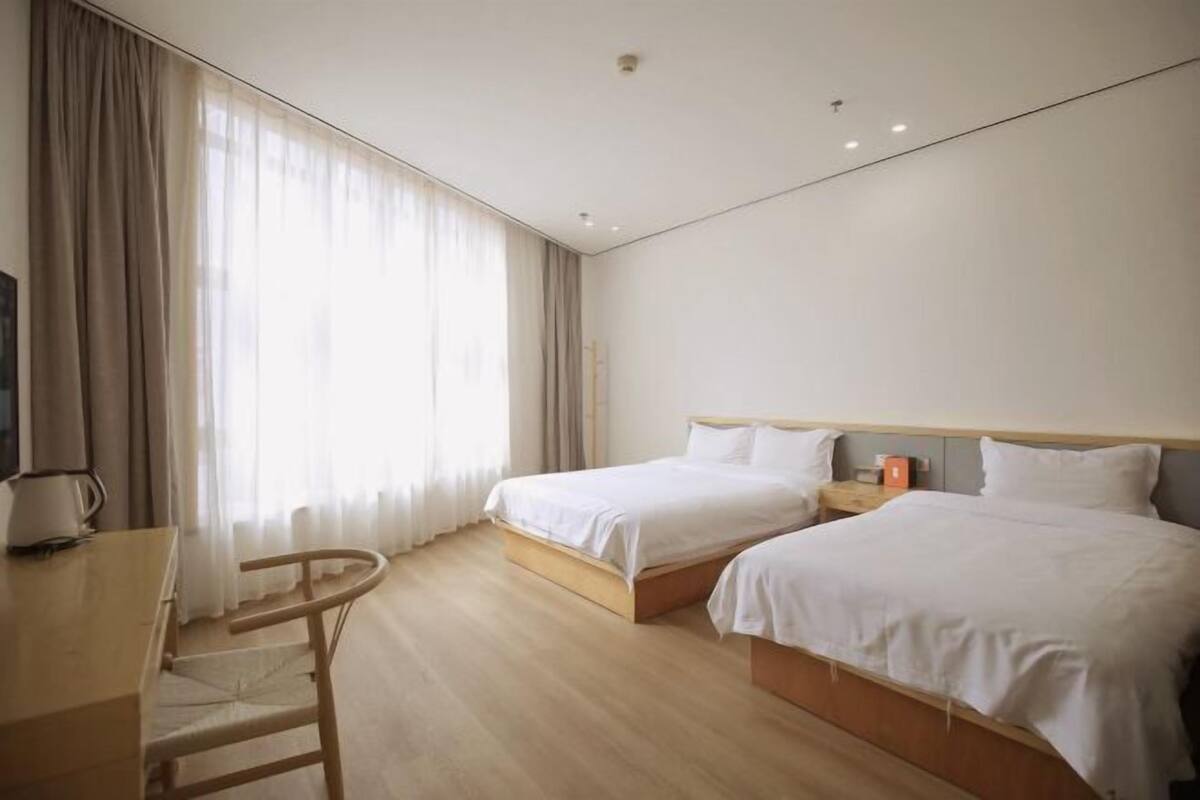Una habitación de hotel con dos camas, un escritorio de madera, una silla y una ventana con cortinas.