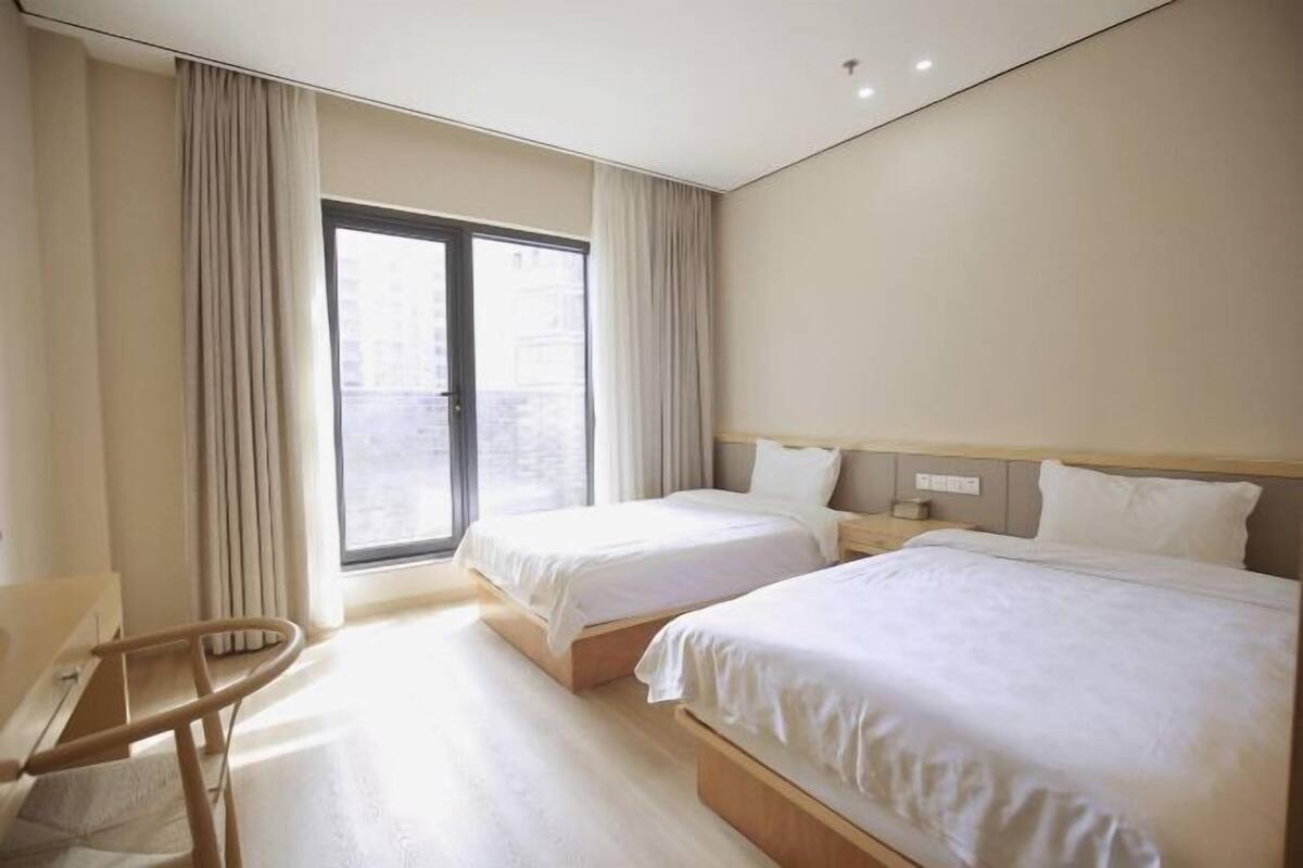 Una habitación de hotel con dos camas, una silla y un ventanal amplio.