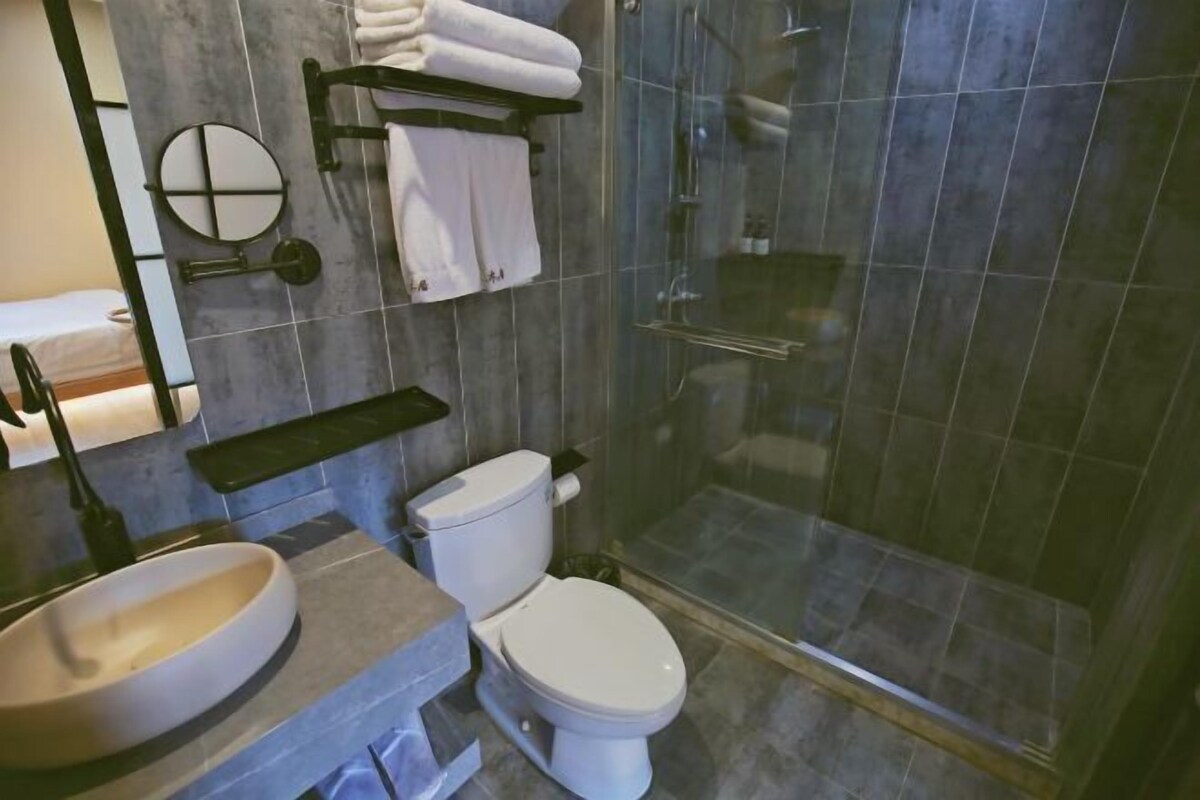 A bathroom with a round mirror, a toilet, a sink, and a glass-enclosed shower.