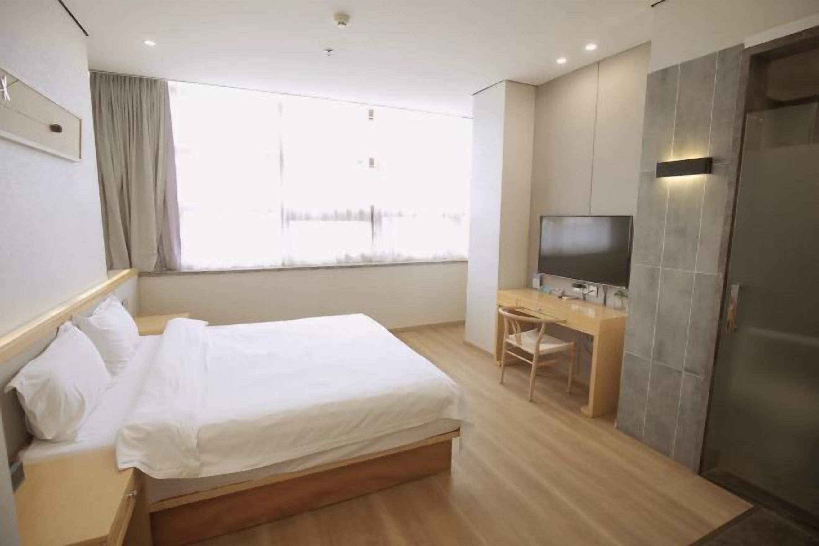 A hotel room with a bed, a desk, a TV, and a wardrobe.