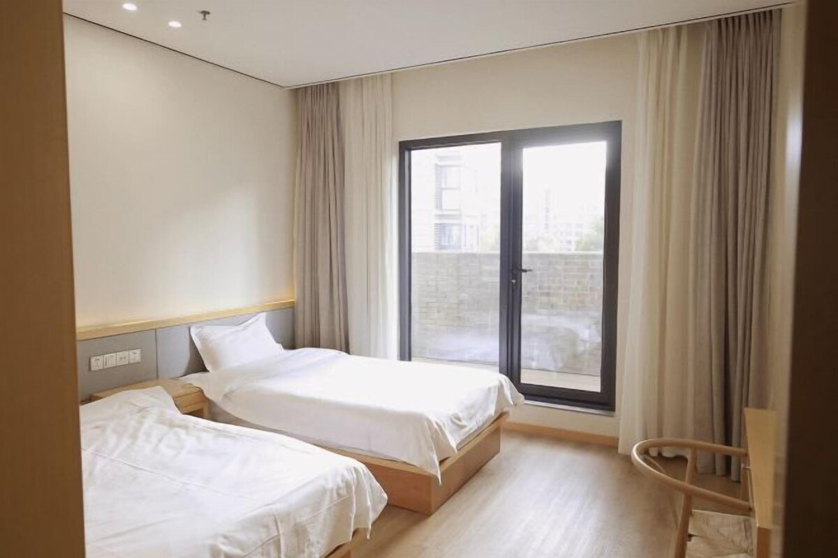 A hotel room with two beds, a large window, and a view of the outside.