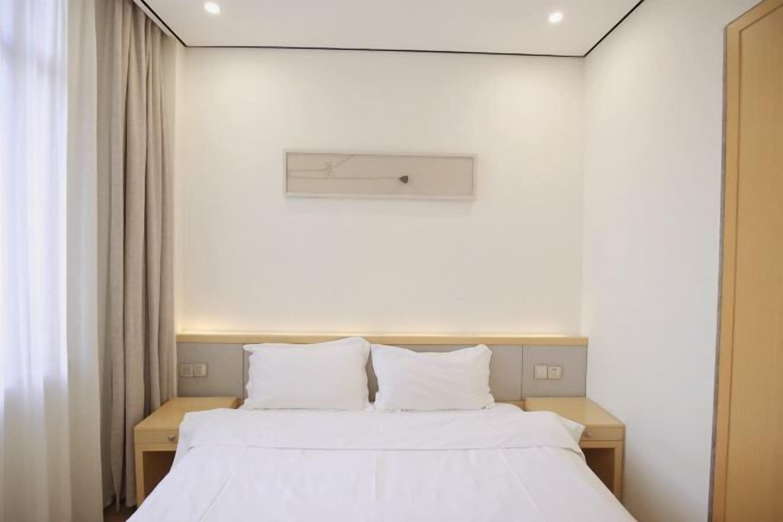 Une chambre d’hôtel comprenant un lit, deux tables de chevet, une tête de lit et un luminaire fixé au mur.