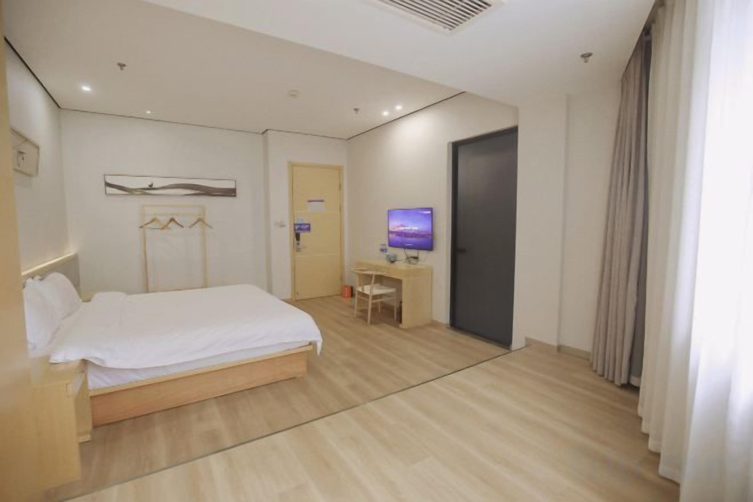 A hotel room with a bed, desk, chair, television, and a door.