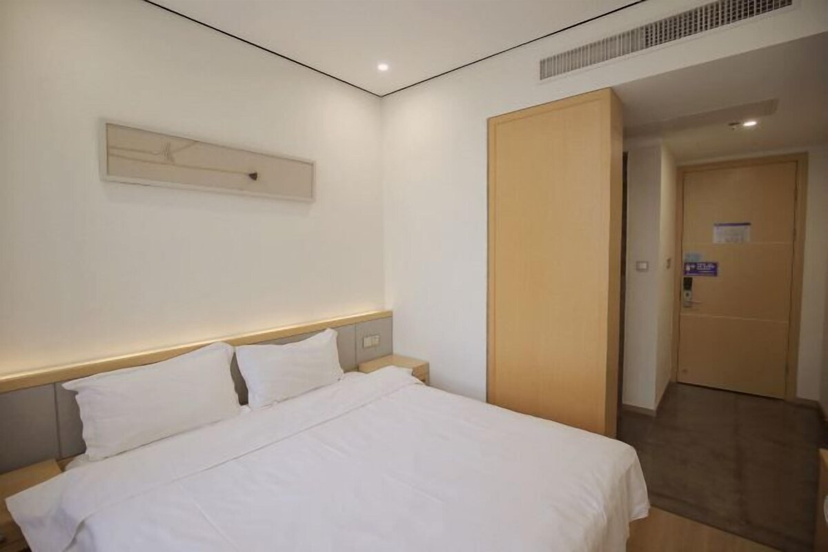 A hotel room with a bed, a nightstand, a wooden door, and a wall-mounted light fixture.
