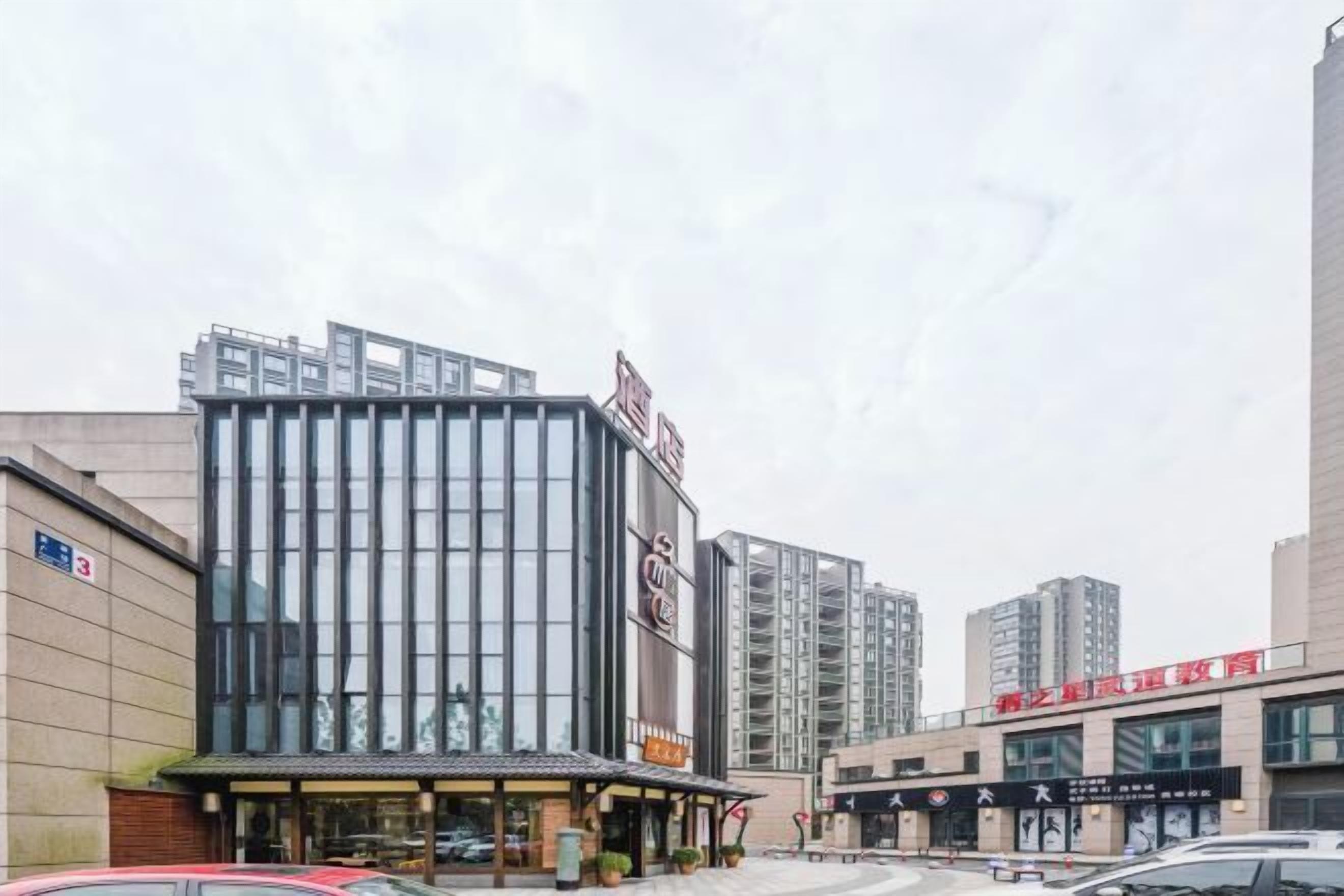 Un bâtiment moderne doté d’une façade en verre, une enseigne avec des caractères chinois et un parking rempli de voitures.