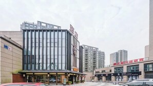 Un edificio moderno con fachada de vidrio, un letrero con caracteres chinos y un estacionamiento con automóviles.
