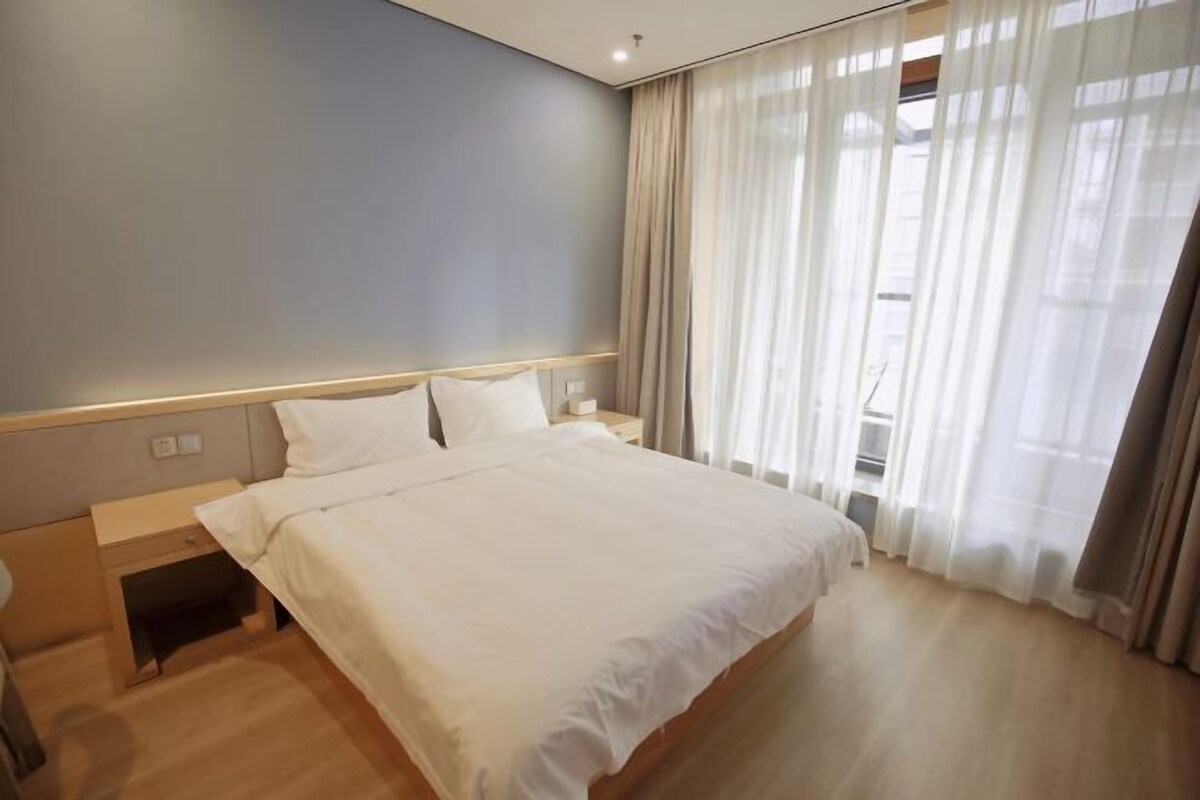 Una habitación de hotel con una cama grande, una mesita de noche, un escritorio y una ventana con cortinas.