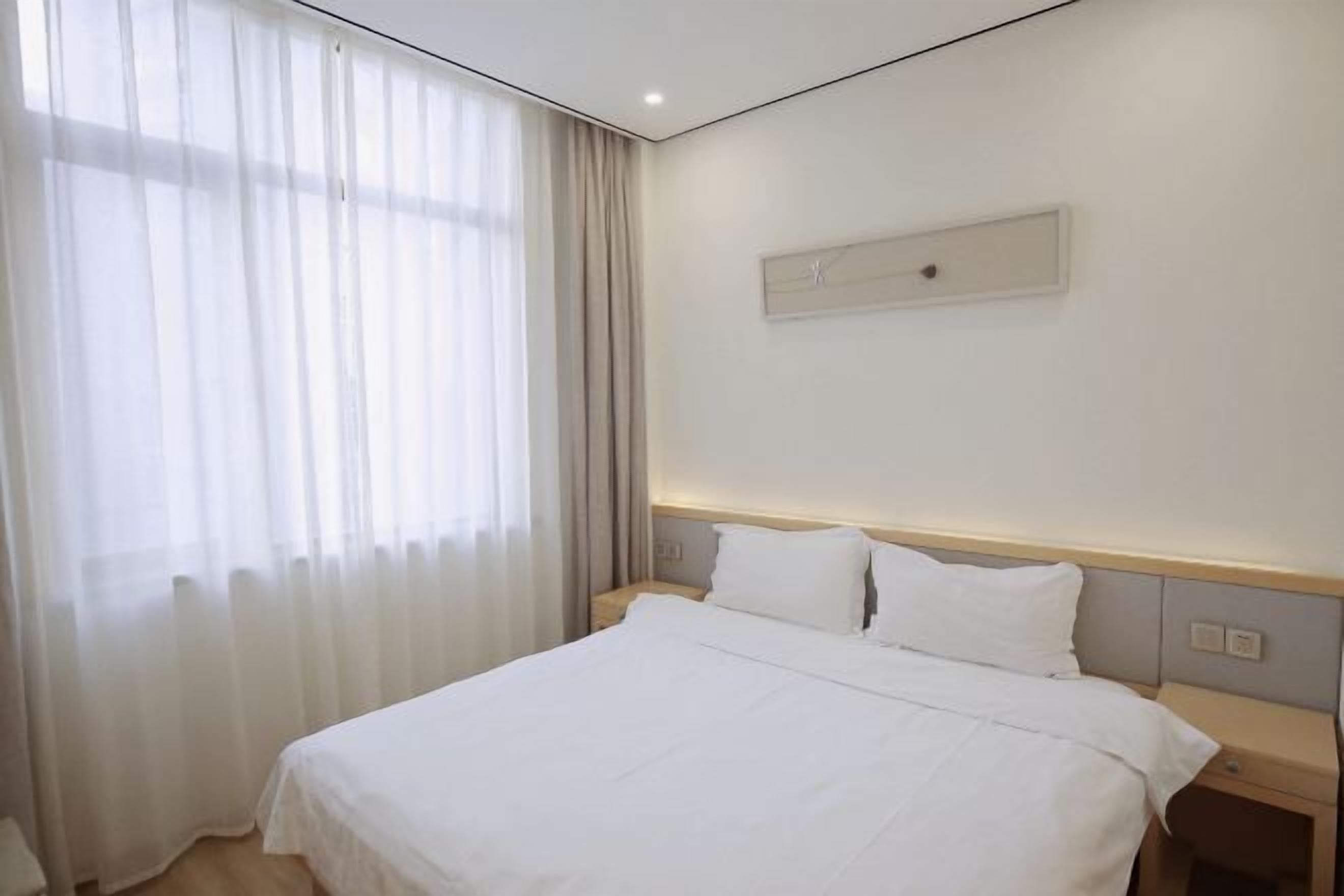 A hotel room with a large bed, a nightstand, and a window with sheer curtains.