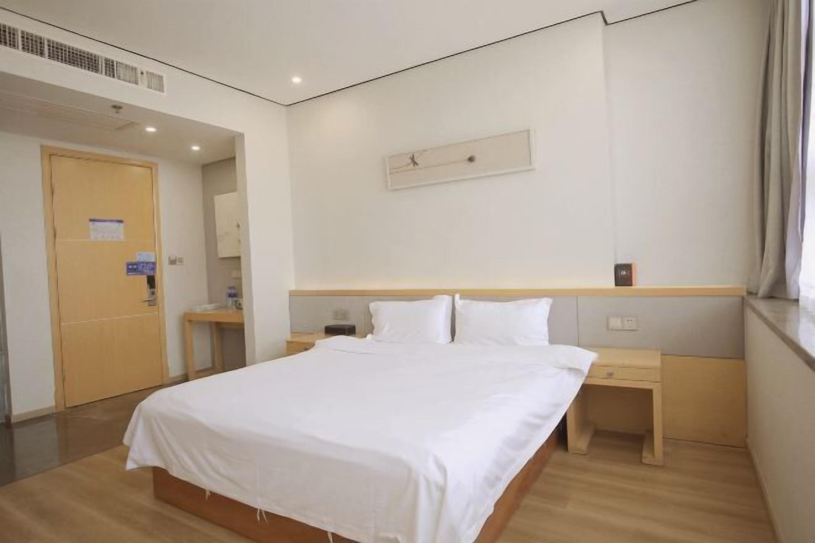 Habitación de hotel con una cama grande, mesitas de noche, un escritorio pequeño y una ventana con cortinas.