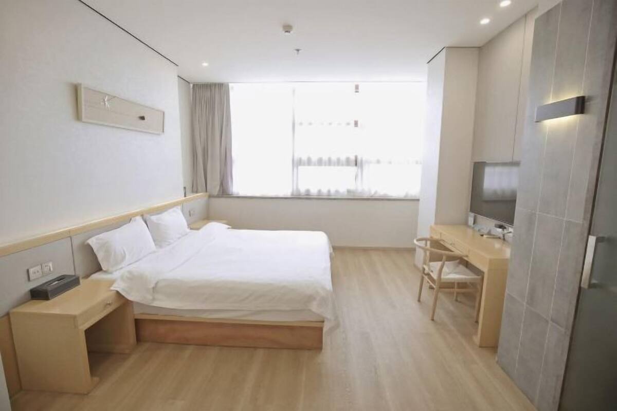 Habitación de hotel con cama, mesita de noche, escritorio, silla, televisor y ventana con cortinas.
