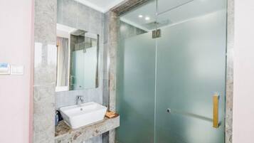 Un baño moderno con cabina de ducha de vidrio, lavabo de mármol y un espejo grande.