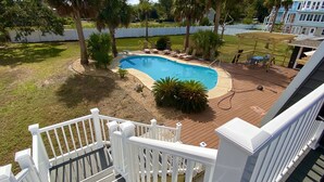 Un jardin avec une piscine, une terrasse en bois et une clôture blanche.