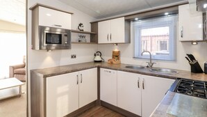 Une cuisine moderne avec des meubles blancs, un four à micro-ondes en acier inoxydable, une cuisinière à gaz et une fenêtre équipée de stores.