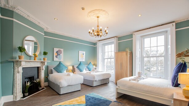 Une chambre d’hôtel avec une cheminée, deux lits, un lustre et de grandes fenêtres.
