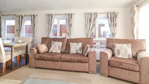 En stue med et brunt sofasæt, et glasbord og et spisebord med stole.