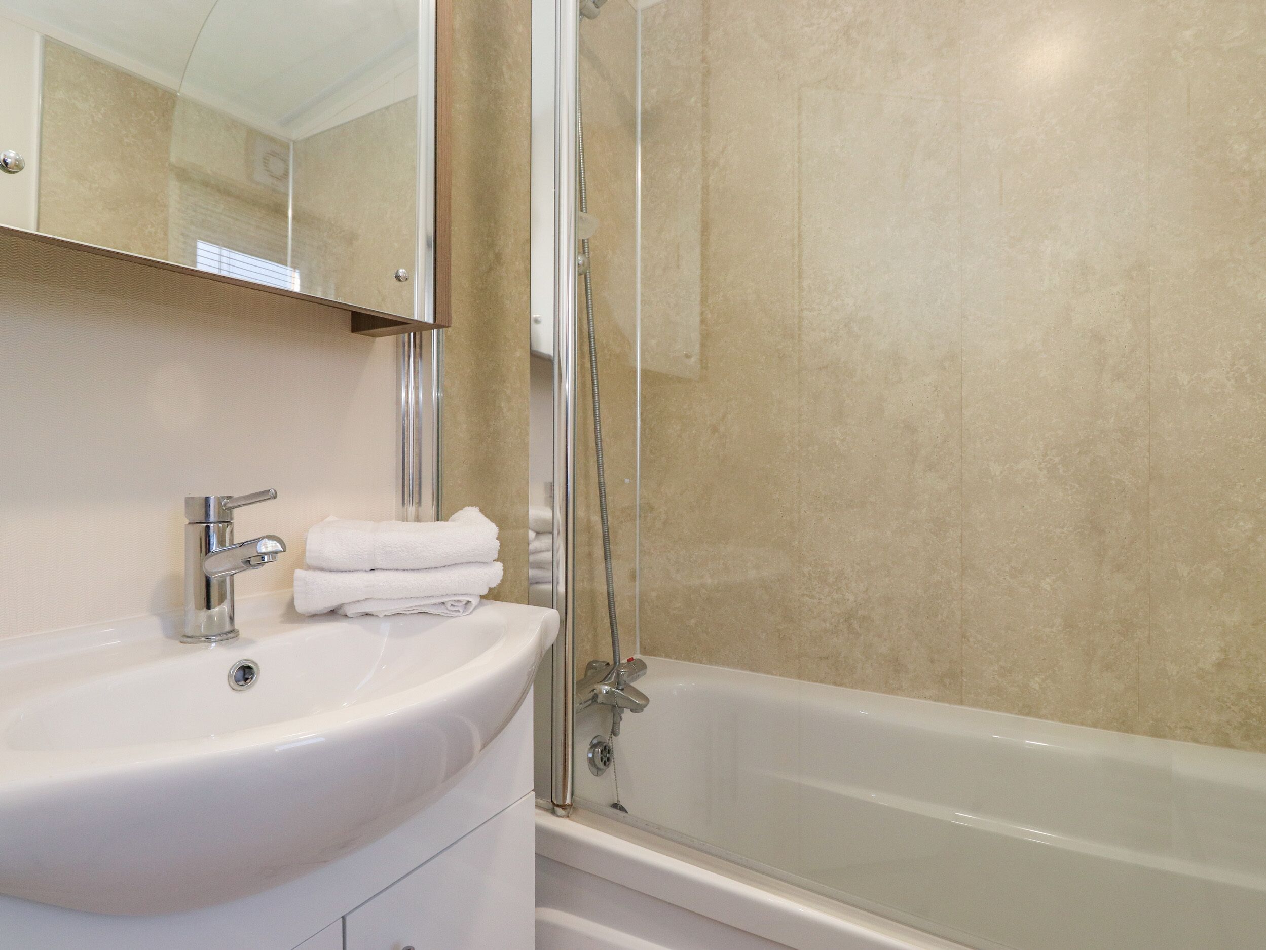 Ett badrum med ett vitt handfat, en spegel och en dusch med glasväggar.