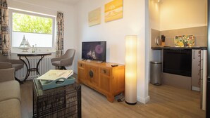 Um espaço habitável compacto com televisão, armário de madeira, mesa de jantar e cozinha equipada com frigorífico e fogão.