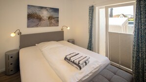 Quarto com cama, luminárias de cabeceira, mesa de cabeceira, janela com cortinas e arte na parede com tema de praia.