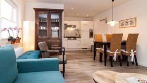 Een moderne woonkamer met een blauwe bank, een eettafel met rieten stoelen en een kast met glazen deuren.