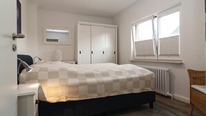 Een slaapkamer met een bed, kledingkast, stoel en een raam met jaloezieën.
