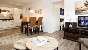 Een moderne woonkamer met een eethoek, houten vloeren en een tv op een houten dressoir.