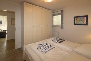 Un dormitorio con una cama, dos mesitas de noche, un armario, una ventana con persianas y un cuadro en la pared.