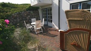 Eine Terrasse mit Korbmöbeln, einer Steinmauer und einem weiß gestrichenen Gebäude mit Balkon.