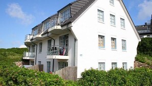 Ein zweistöckiges Haus mit einem Balkon im oberen Stockwerk, umgeben von viel Grün.